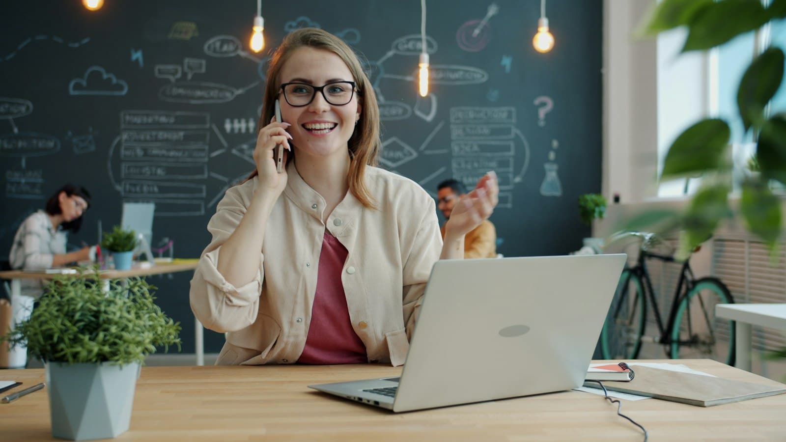 A woman smiling while talking on the phone at a desk with a laptop